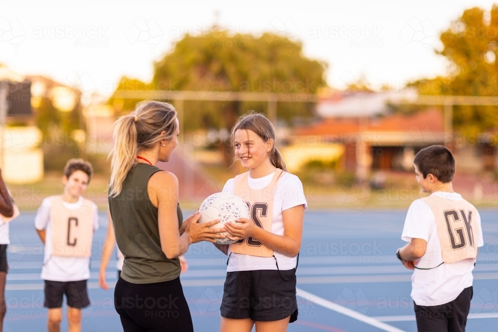 netball coach interacting with girl holding ball at netball training - Australian Stock Image