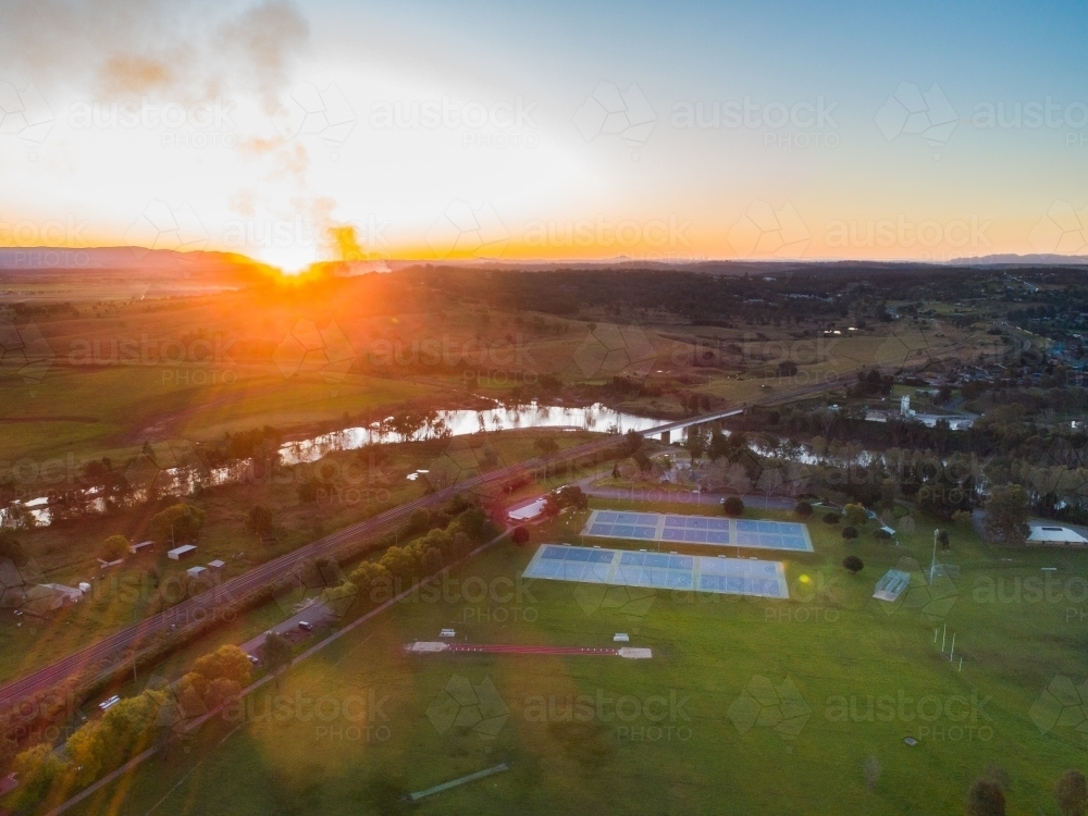 Netball courts in park beside river at sunset with smoke in sky - Australian Stock Image