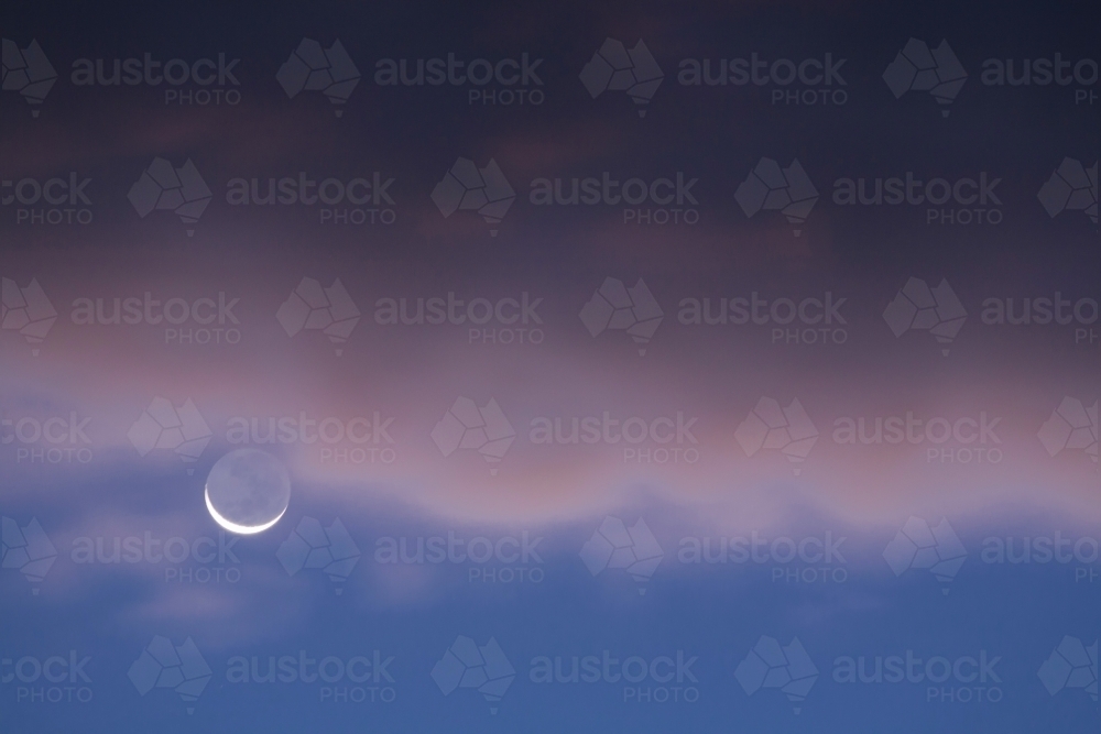 New moon with blue evening sky and coloured clouds - Australian Stock Image