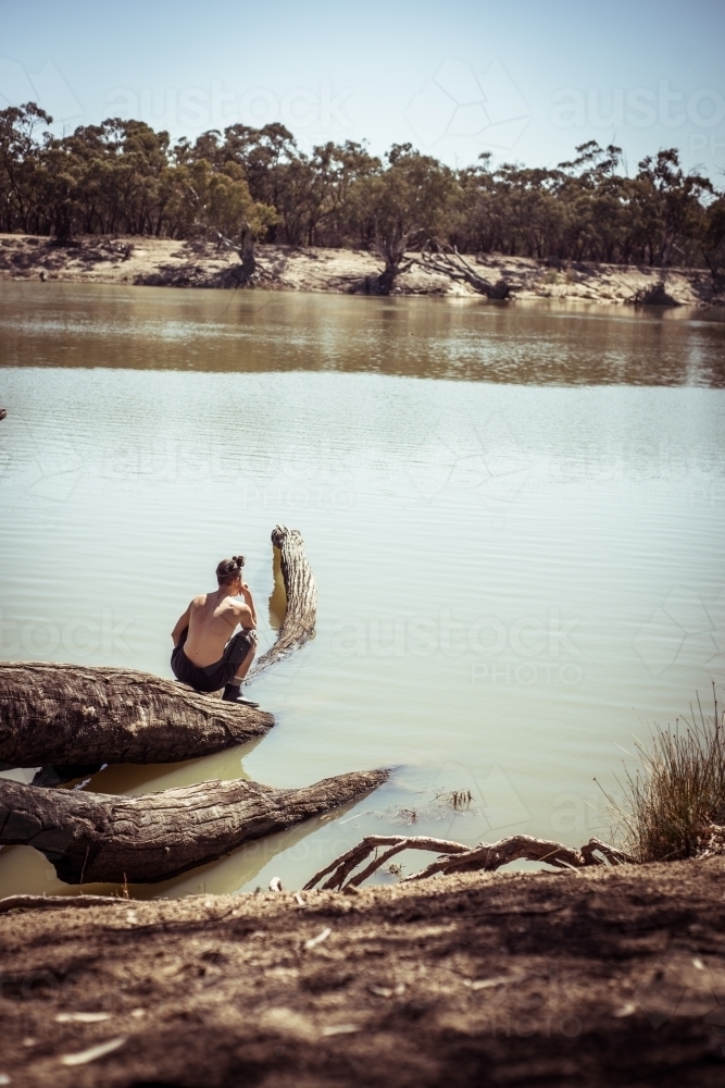 Person squatting on a log that is immersed in a river - Australian Stock Image