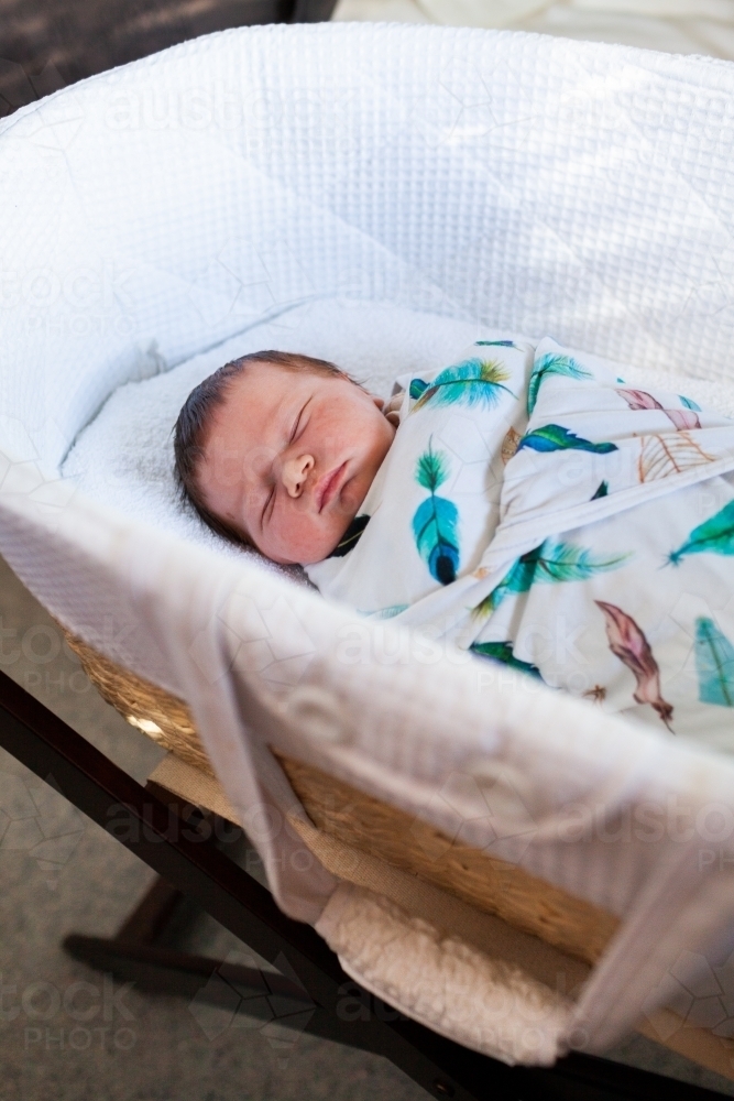 Newborn baby wrapped up in blanket in bassinet asleep - Australian Stock Image