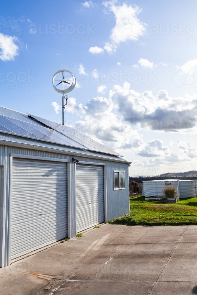 Off grid sustainable living with wind turbine power generator and solar panels on shed roof - Australian Stock Image