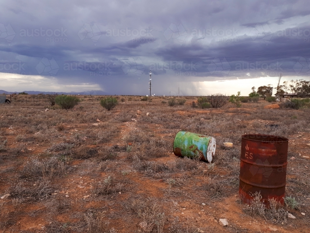 old barrels in barren landscape with storm in background - Australian Stock Image