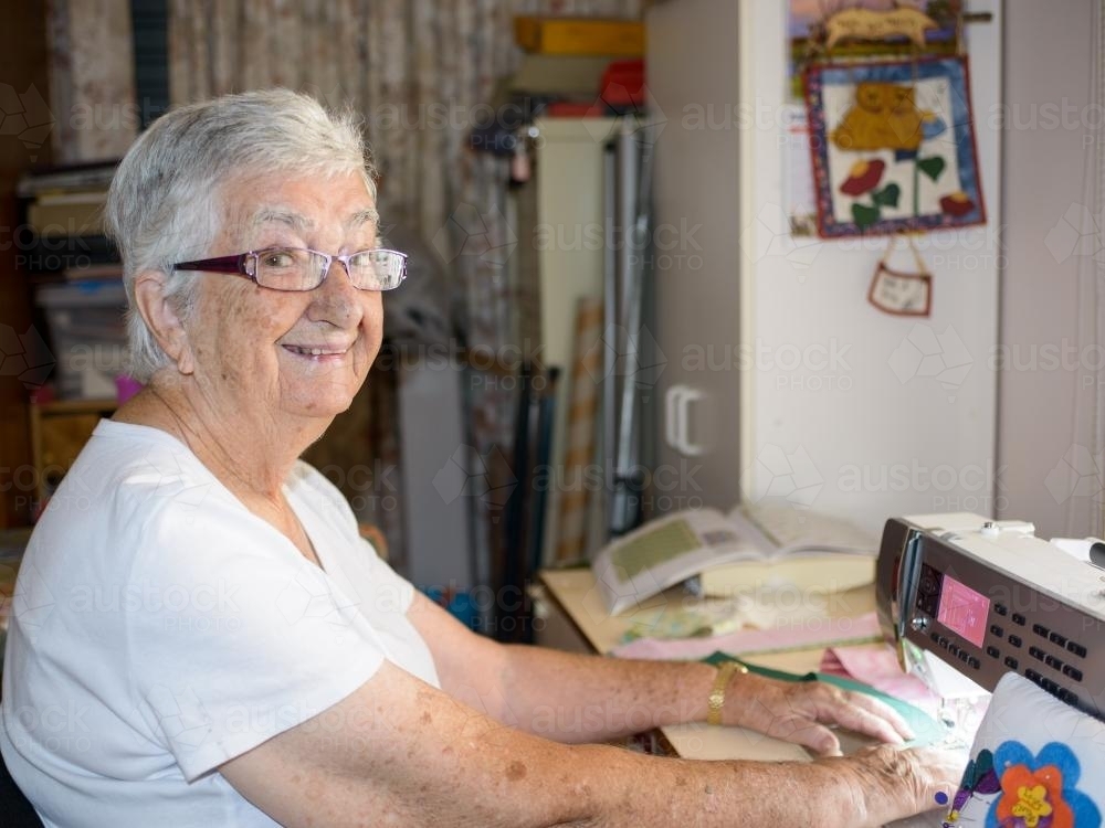 Old grey haired woman at modern sewing machine - Australian Stock Image