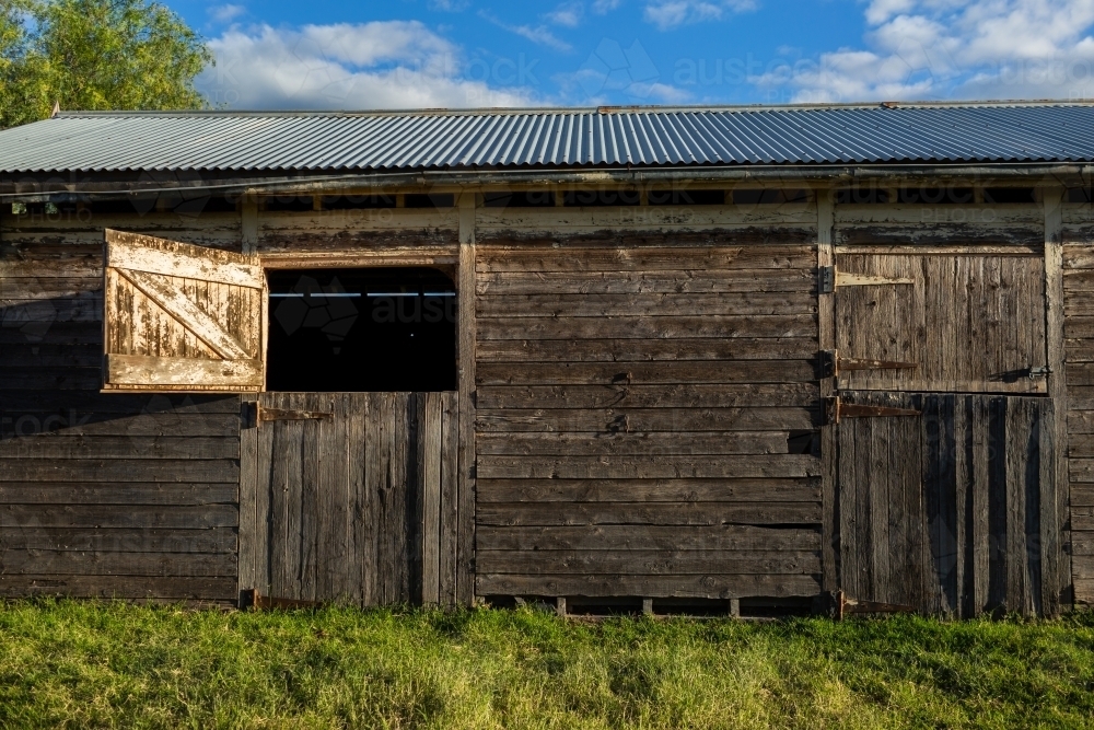 Old weather worn structure of wooden stables on farm in sunlight - Australian Stock Image