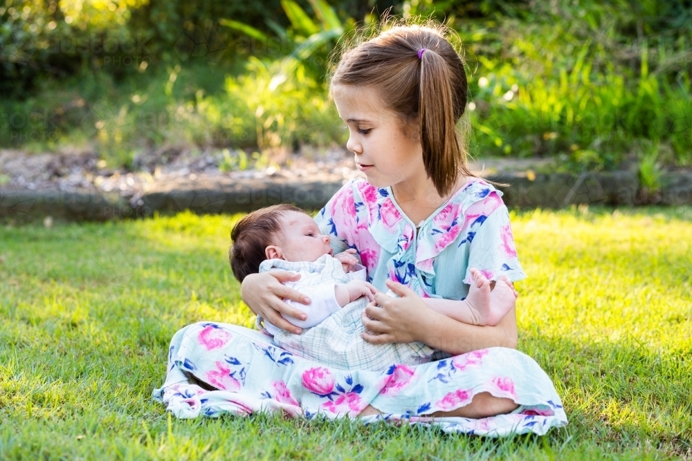 Older child cuddling young baby girl outside - loving family interaction - Australian Stock Image