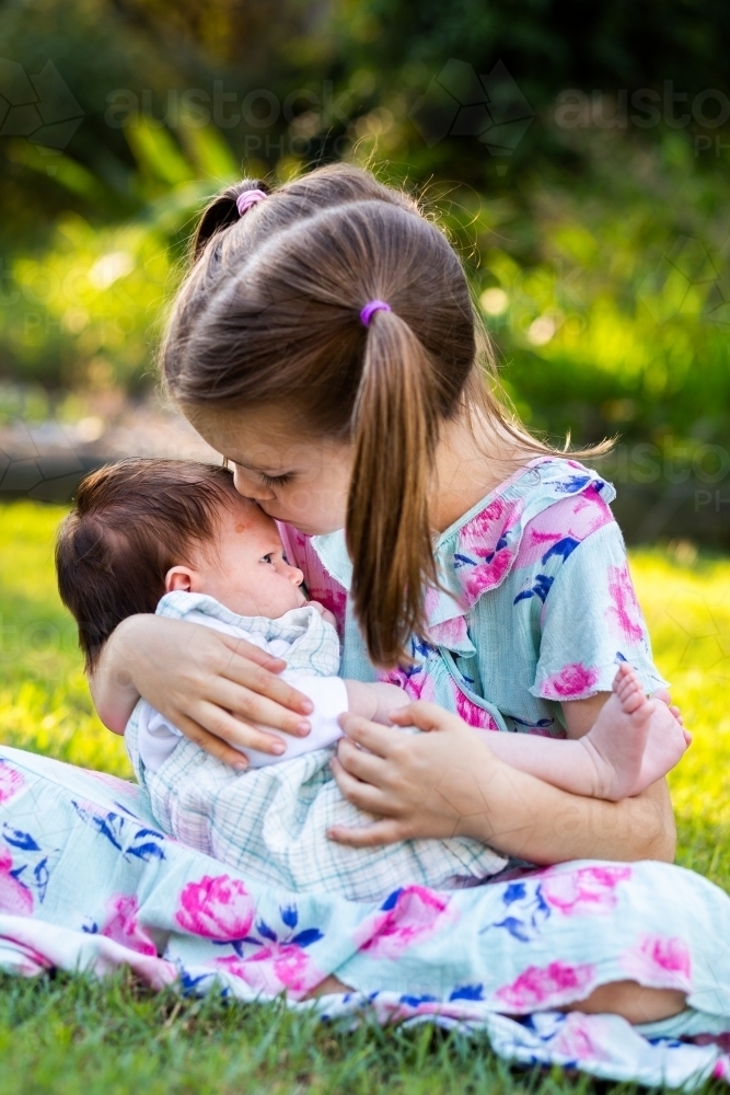 Older child cuddling young baby girl outside - loving family interaction - Australian Stock Image