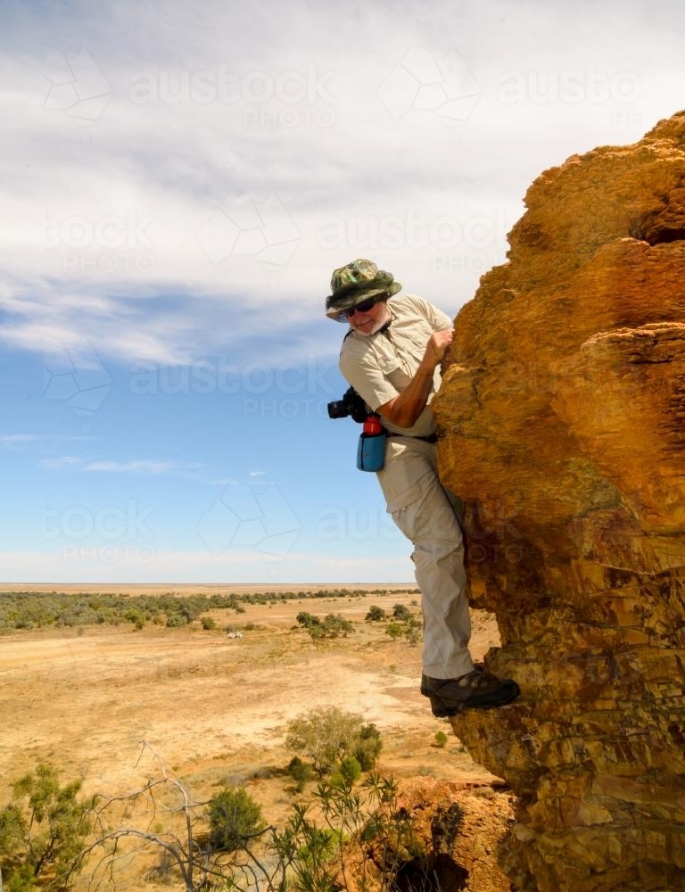 Older man climbing on cliff and looking down - Australian Stock Image