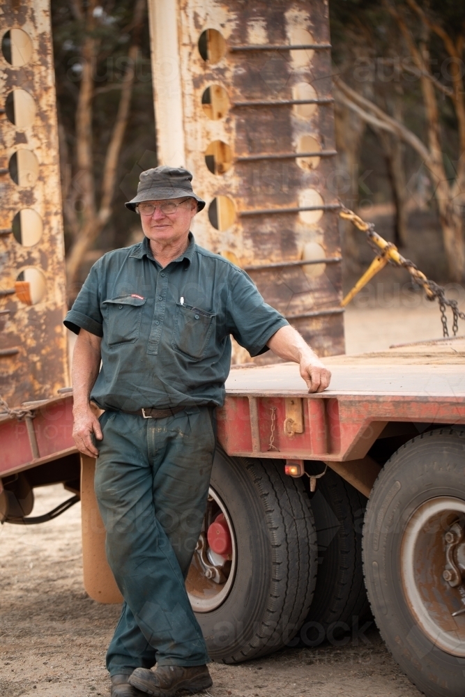 Older worker in dark green workwear standing next to truck - Australian Stock Image