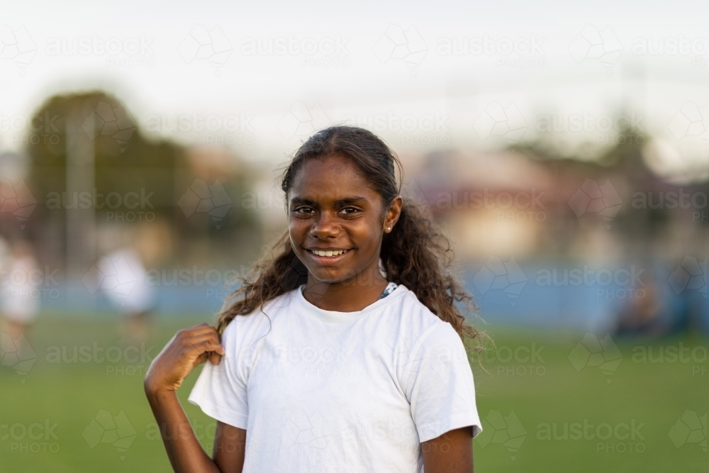 one aboriginal girl by herself wearing a white tee shirt against a blurry suburban background - Australian Stock Image