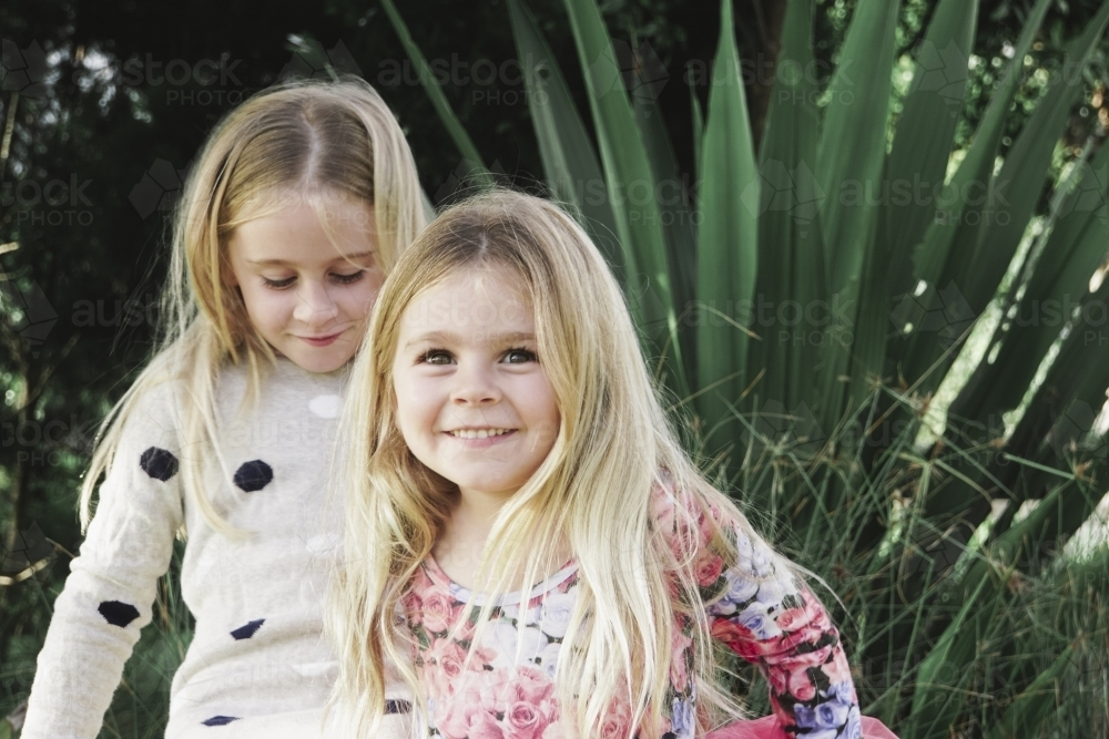 One girl looking down, one girl smiling while playing outdoors - Australian Stock Image