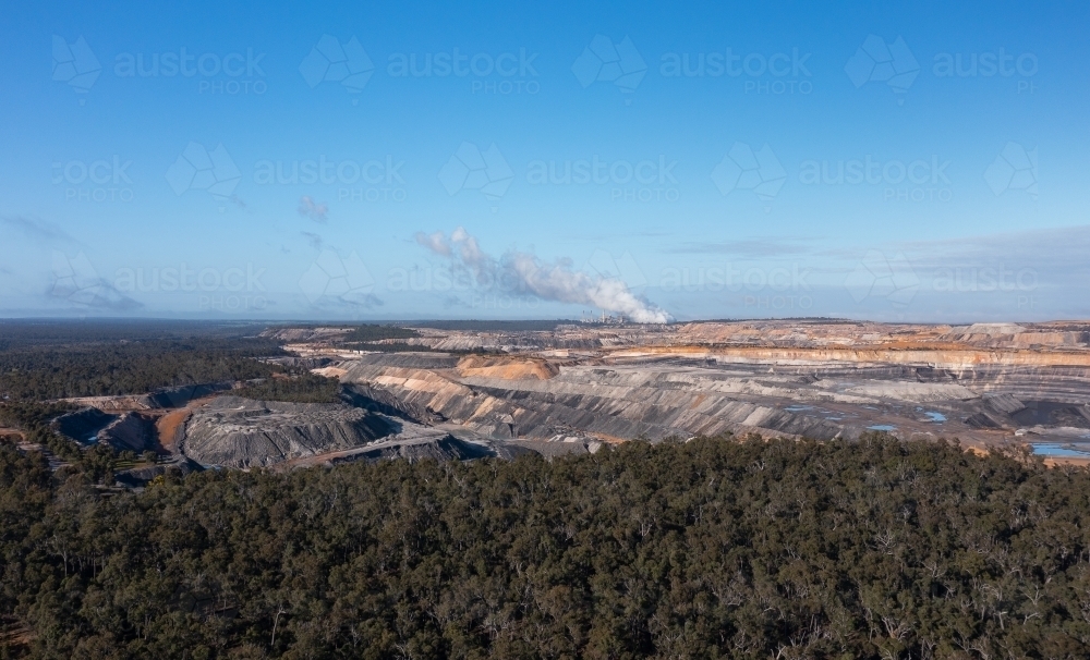 open cut coal mine with coal-fired power station on horizon and native forest in foreground - Australian Stock Image