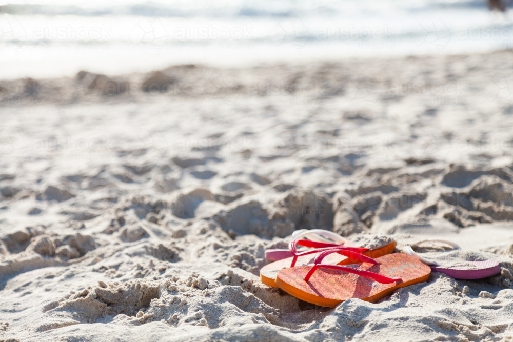 Orange and pink thongs left on sand at busy beach - Australian Stock Image