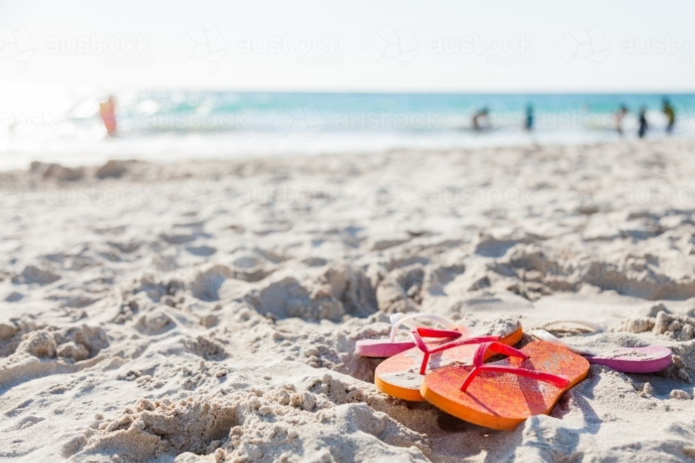 Orange and pink thongs left on sand at busy beach - Australian Stock Image