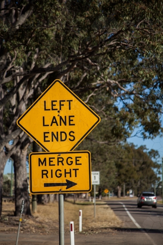 Orange left lane ends merge right sign with an arrow on the roadside - Australian Stock Image