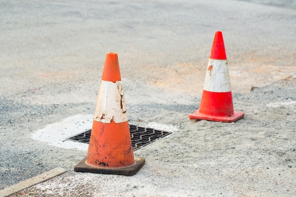 Orange traffic cones and drain hole on road surface - Australian Stock Image