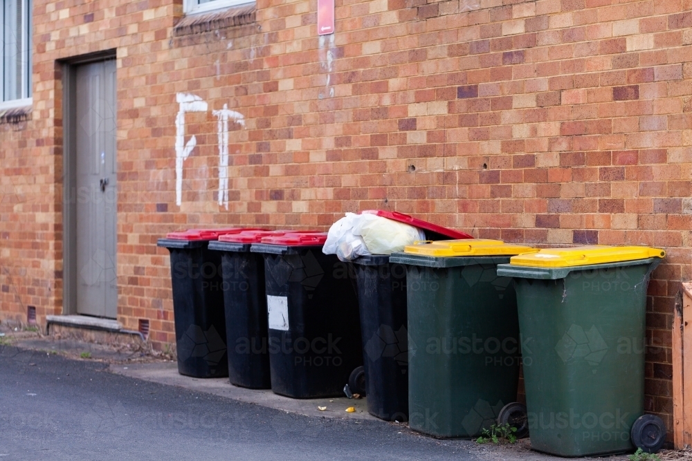 Overflowing trash in rubbish bin lined up on wall - Australian Stock Image