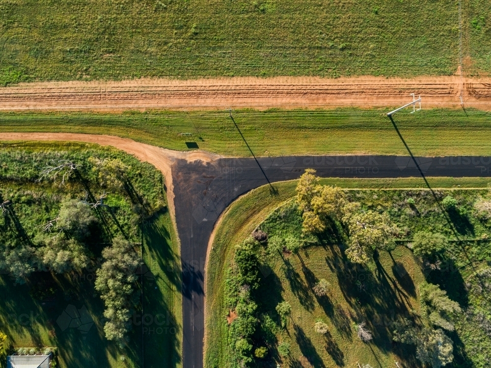 Overhead aerial view of right angled bend in country road beside farmland - Australian Stock Image