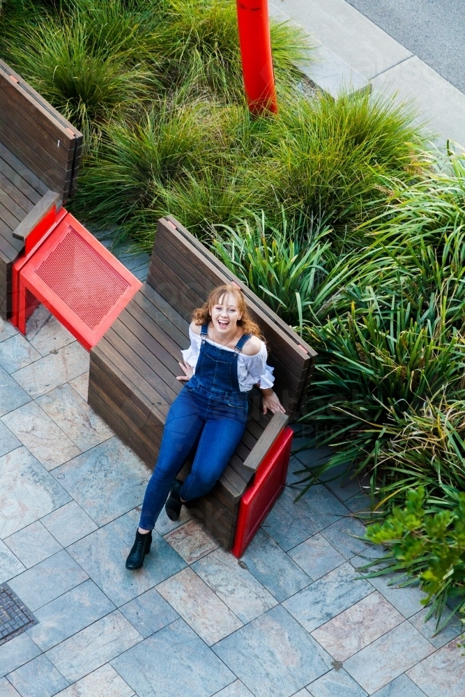 Overhead photo of young woman seated on bench seat on footpath - Australian Stock Image