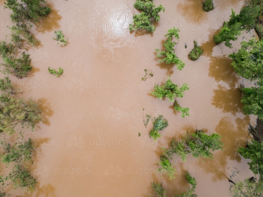 Overhead view of rushing brown floodwaters overflowing river bank - Australian Stock Image