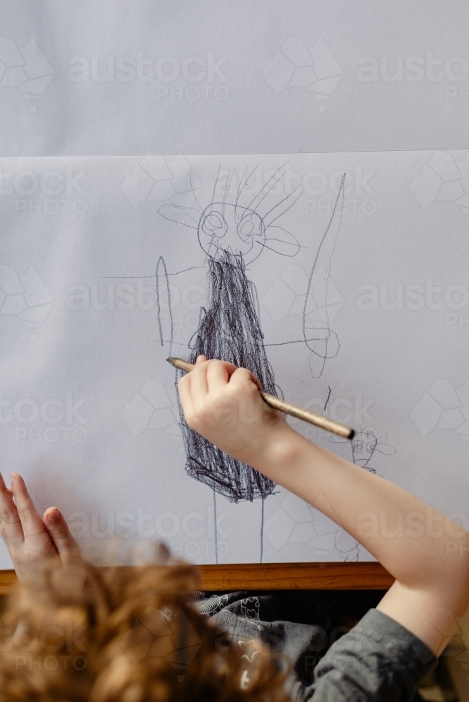 Overhead view of child's drawing a figure with a pencil - Australian Stock Image