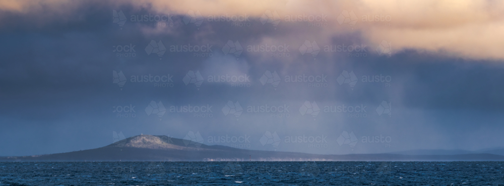 Panoramic view of rain falling from clouds in a dark sky over a distant coastline - Australian Stock Image