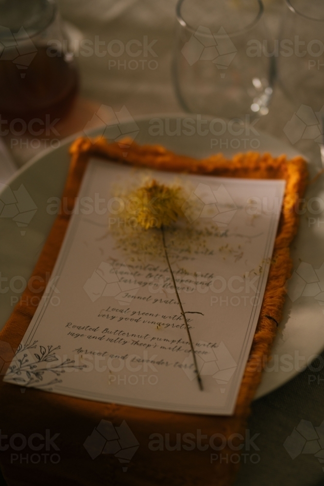 Paper menu on top of the orange napkin with dried yellow flower resting on it - Australian Stock Image