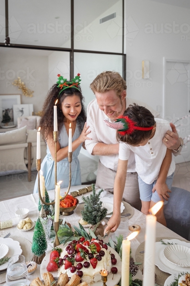 Parents helping son slice pavlova at Christmas dinner table - Australian Stock Image