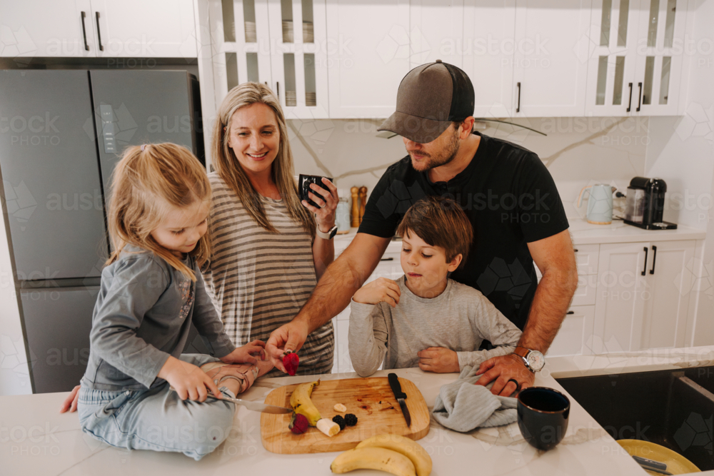 Parents teaching kids how to cut fruits in the kitchen. - Australian Stock Image