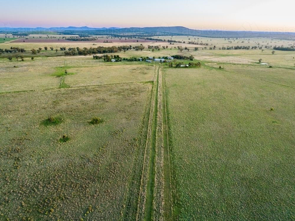 Pastoral farm pastures with trail leading to farm buildings and house at dusk - Australian Stock Image