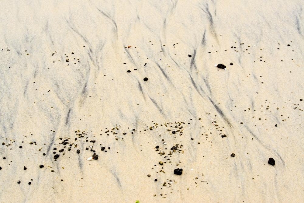 Patterns in wet yellow and black mineral sands on a beach at low tide with pebbles - Australian Stock Image