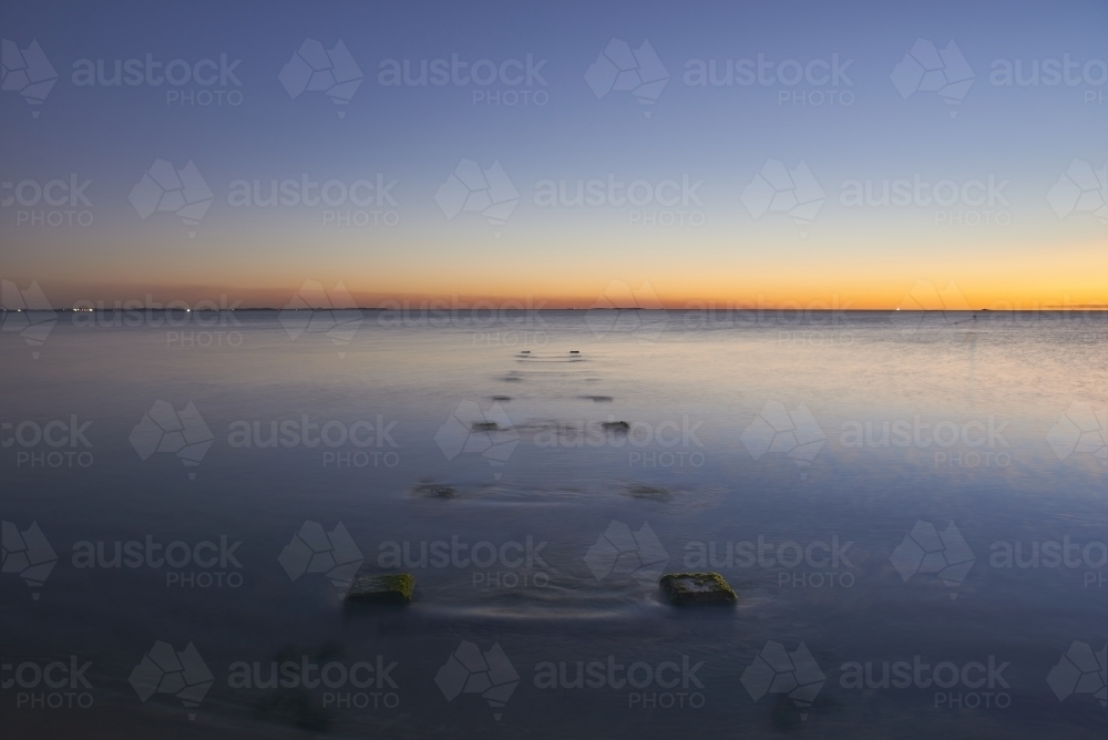 Peaceful ocean at dusk with jetty ruins protruding from the still water. - Australian Stock Image