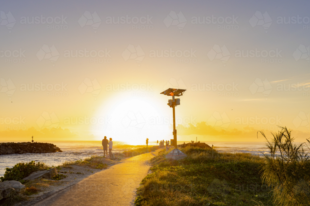 People walking along rock wall at sunrise with the ocean waves breaking on both sides - Australian Stock Image