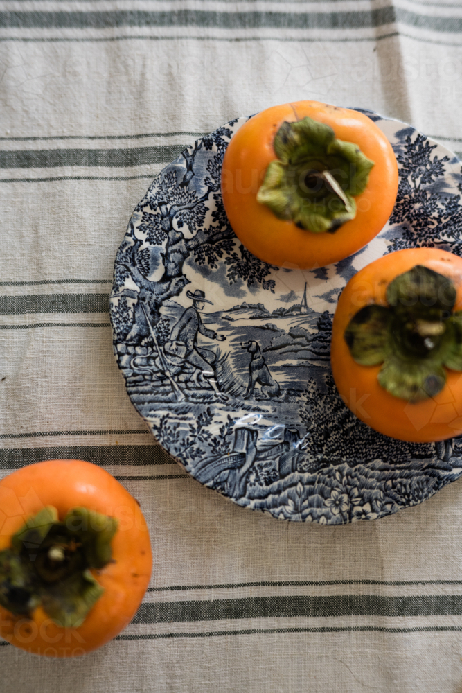 persimmons on a blue and white plate - Australian Stock Image