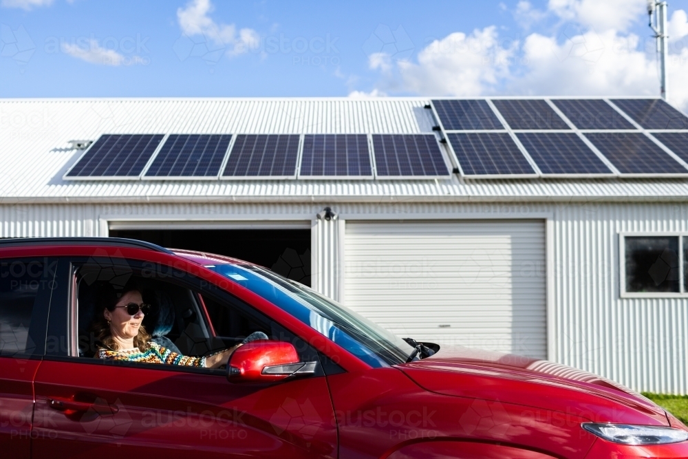 Person driving ev car with solar panels on roof in background - sustainable living - Australian Stock Image