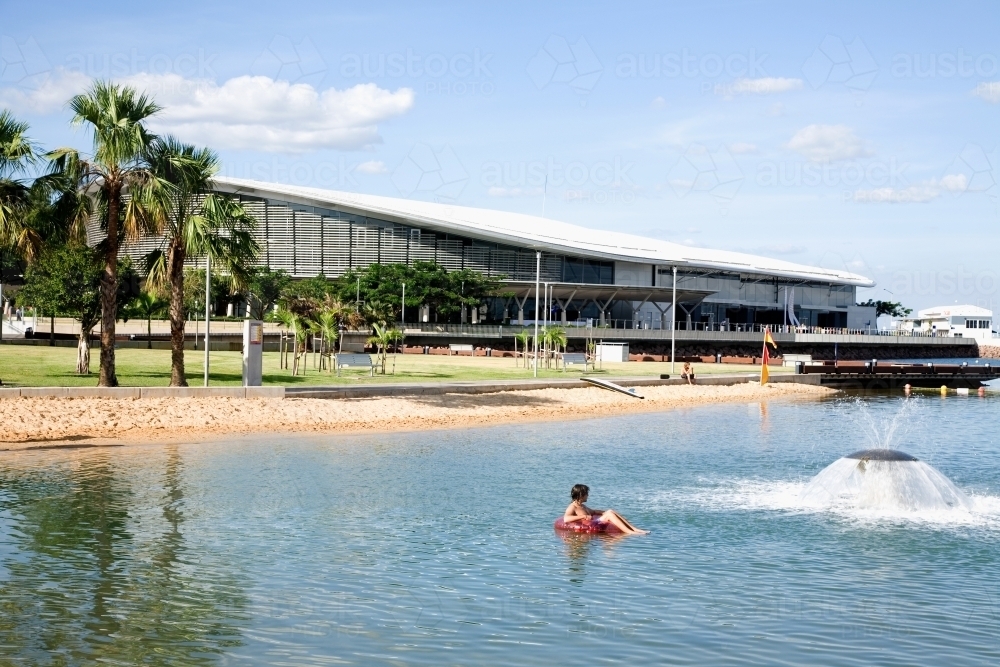 Person floating in Darwin lagoon with Convention Centre in background - Australian Stock Image