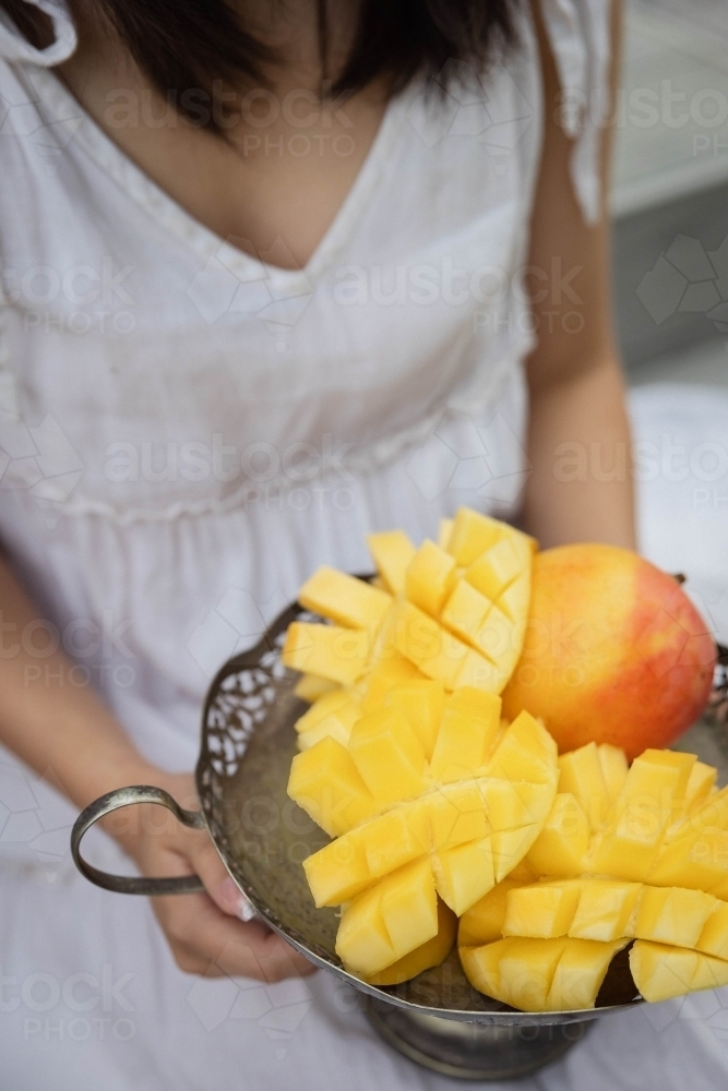 Person holding bowl of cut-up mango - Australian Stock Image