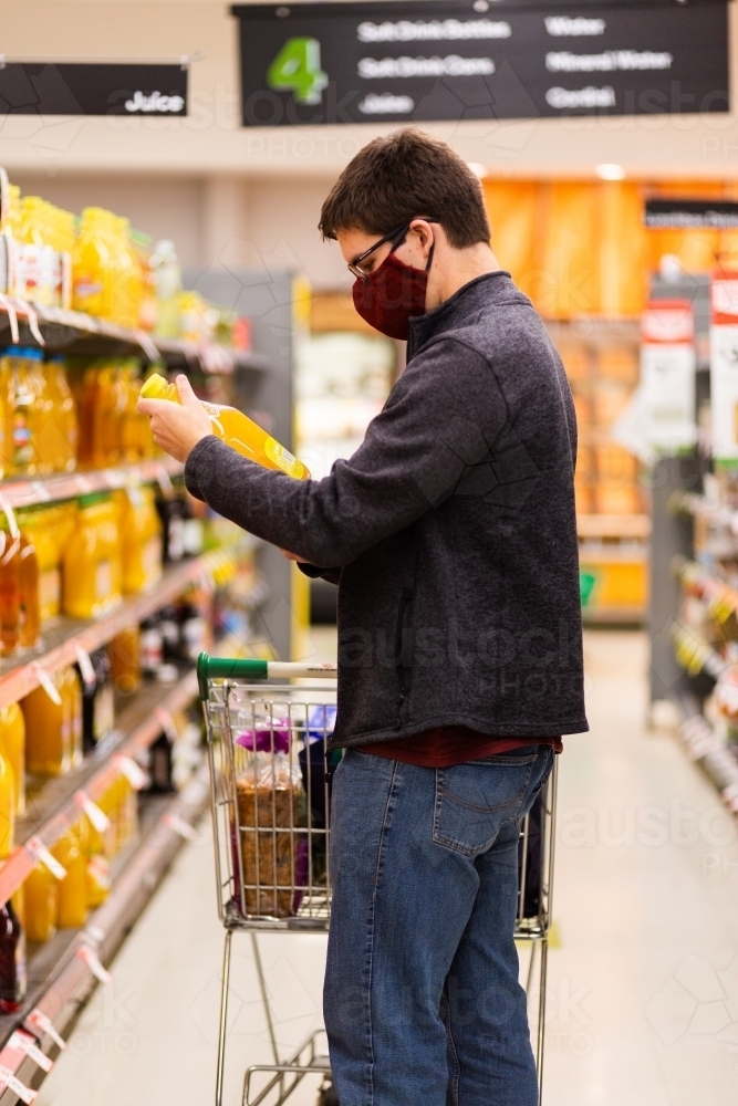 person in grocery store aisle buying juice wearing home made face mask during covid-19 pandemic - Australian Stock Image