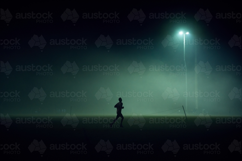 Person playing on sport oval in fog at night - Australian Stock Image