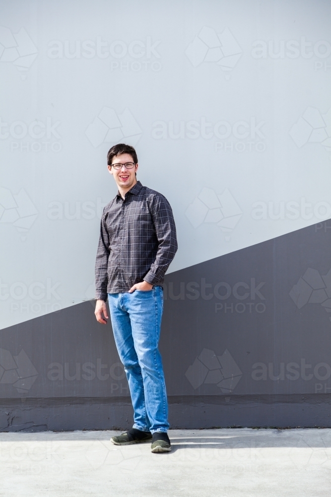 Person standing beside wall in urban area - full length body shot of young man - Australian Stock Image