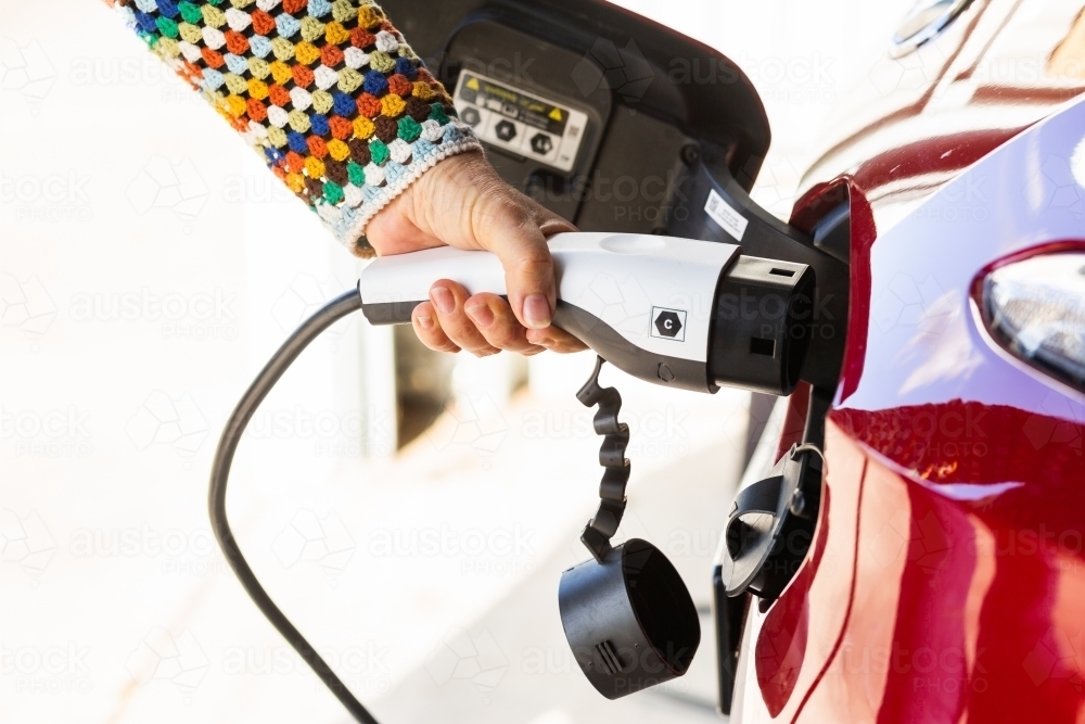 Person unplugging electric vehicle charging plug ready to travel - Australian Stock Image