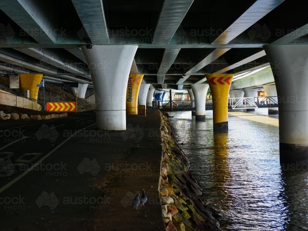 Person walking on the banks of a river under an expressway - Australian Stock Image