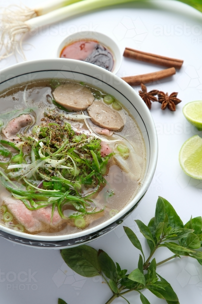 Pho noodle soup in a bowl with fresh herbs and spices on the surface - Australian Stock Image