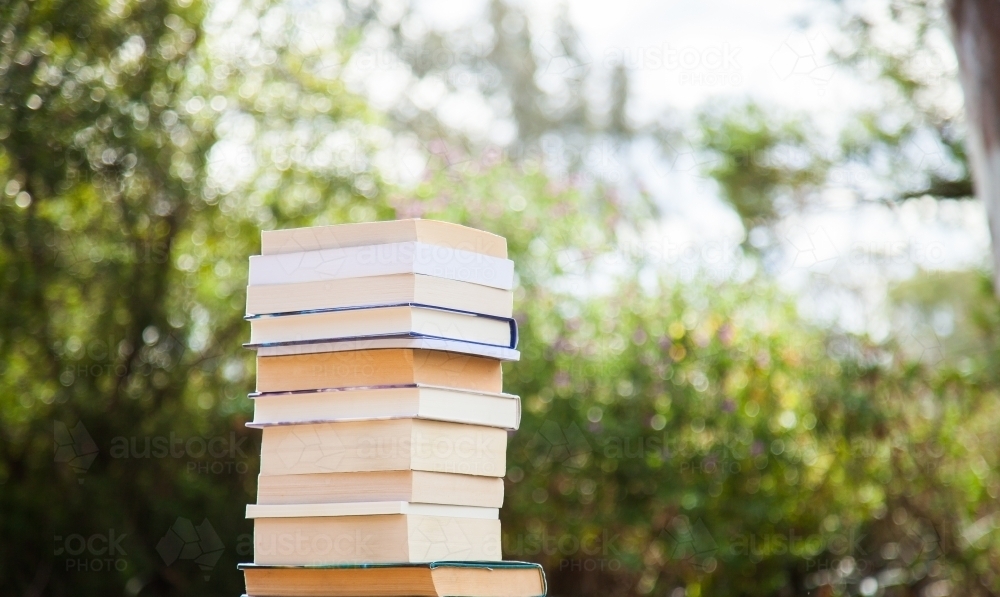 Pile of books outside with green bokeh background - Australian Stock Image