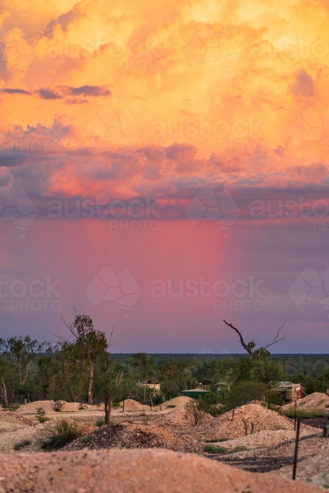 Pink rain falling from a large thunderstorm over an outback mining landscape at sunset - Australian Stock Image