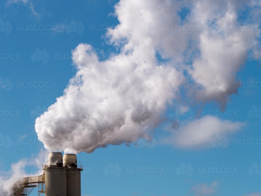 Plumes of steam rising from industrial chimneys into a blue sky - Australian Stock Image