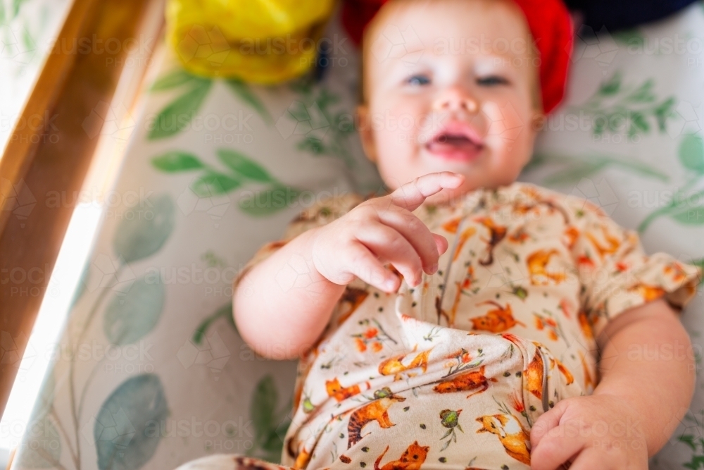 Pointing finger of baby lying on change table ready to get dressed for day - Australian Stock Image