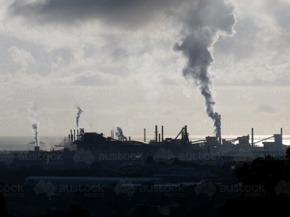 Port Kembla Steel Works silhouetted in the distance emitting steam - Australian Stock Image