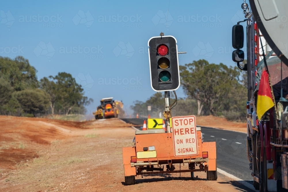 Portable traffic lights set up on the roadside with machinery working in the distance - Australian Stock Image