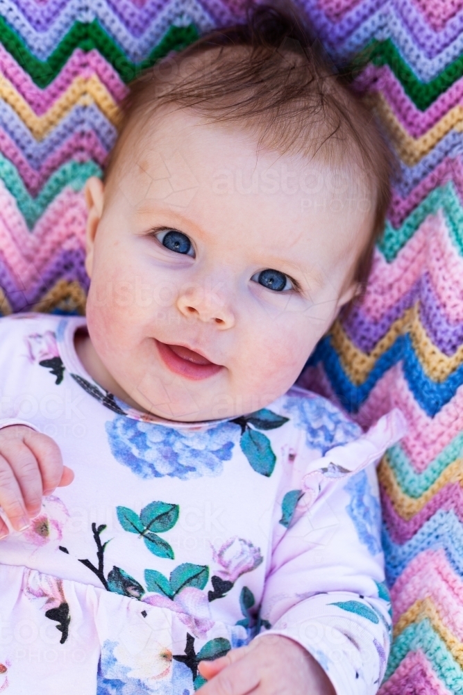 Portrait of a happy four month old baby on pink zigzag blanket - Australian Stock Image